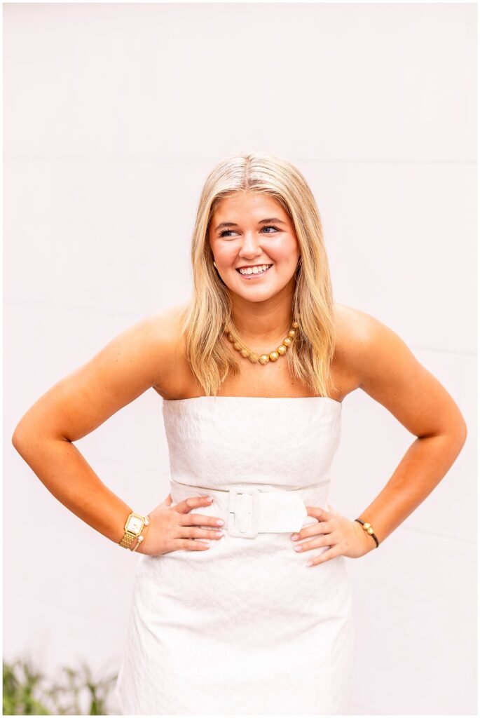 Senior girl laughing over her shoulder in a white dress during her Charleston, SC senior photo session on Meeting Street.