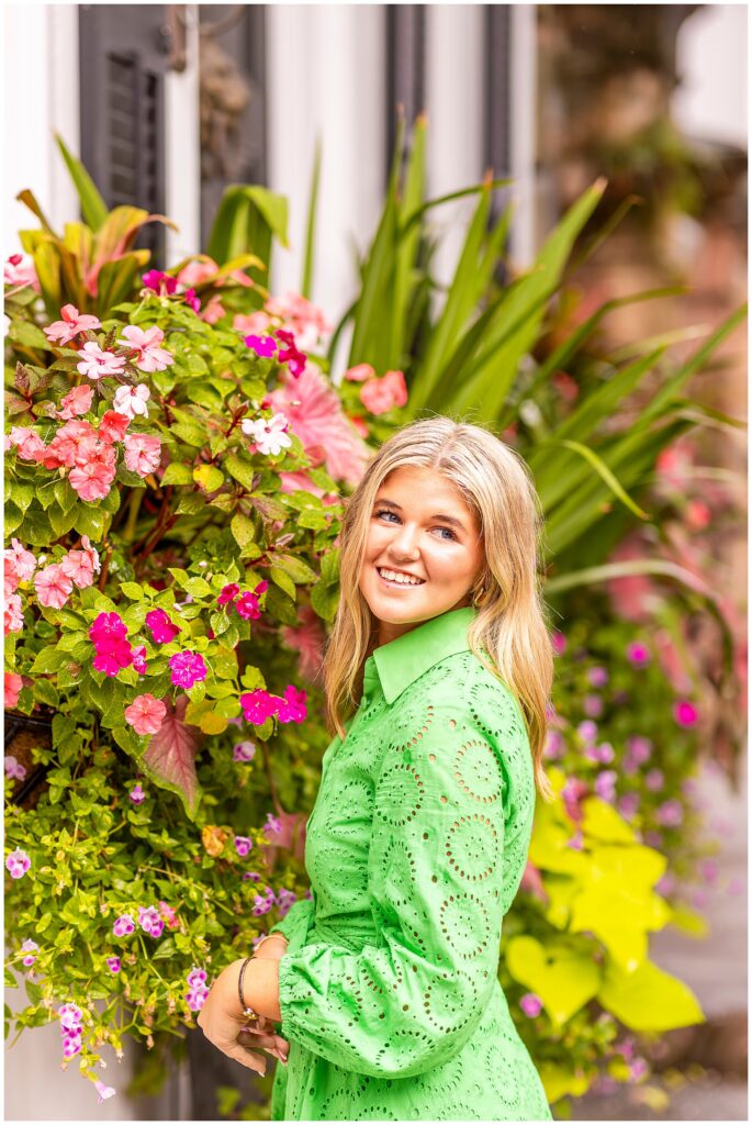 Chic senior portraits in Charleston SC featuring a senior girl in a green dress surrounded by colorful flower boxes and warm light.