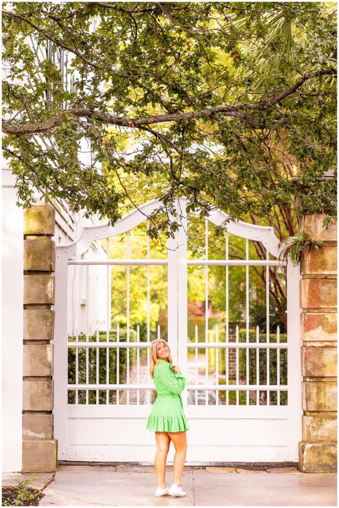 Elegant senior photo of a girl in a green dress smiling softly in front of Charleston’s historic homes on Meeting Street.