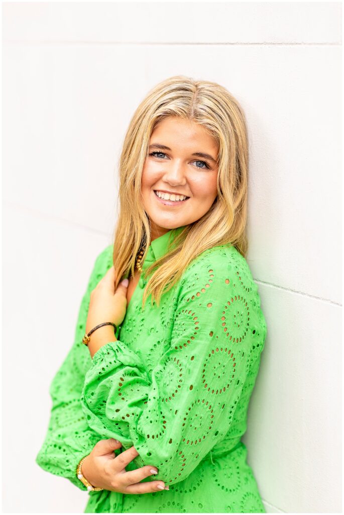 Elegant senior photo of a girl in a green dress smiling softly in front of Charleston’s historic homes.