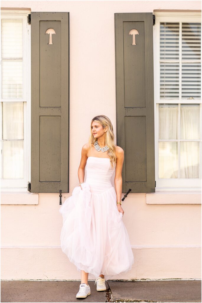 Bella posing in front of a pink Charleston home on Tradd Street, captured in natural morning light.