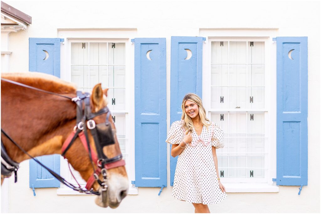 Bella standing near a historic home on Tradd Street with morning light creating a soft glow for her senior session while a horse goes by.