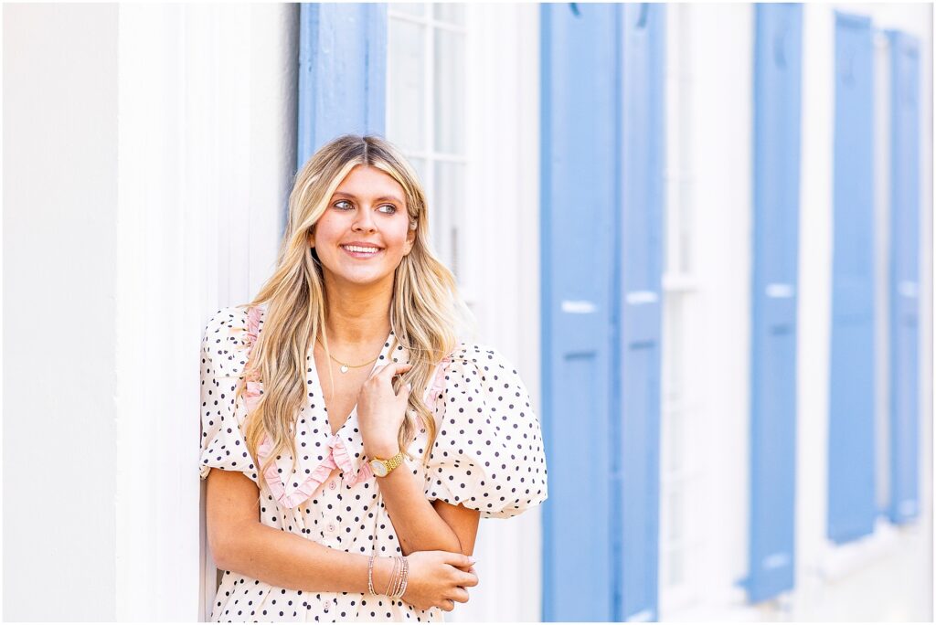 Bella seated on a garden wall near Rainbow Row with sunlight filtering through surrounding trees.