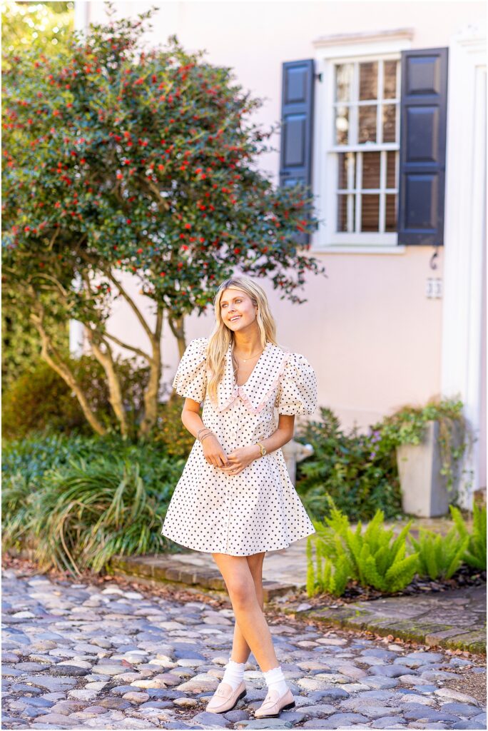 Bella standing in morning sunlight on a quiet Tradd Street, birthday glow on her face during her senior session.
