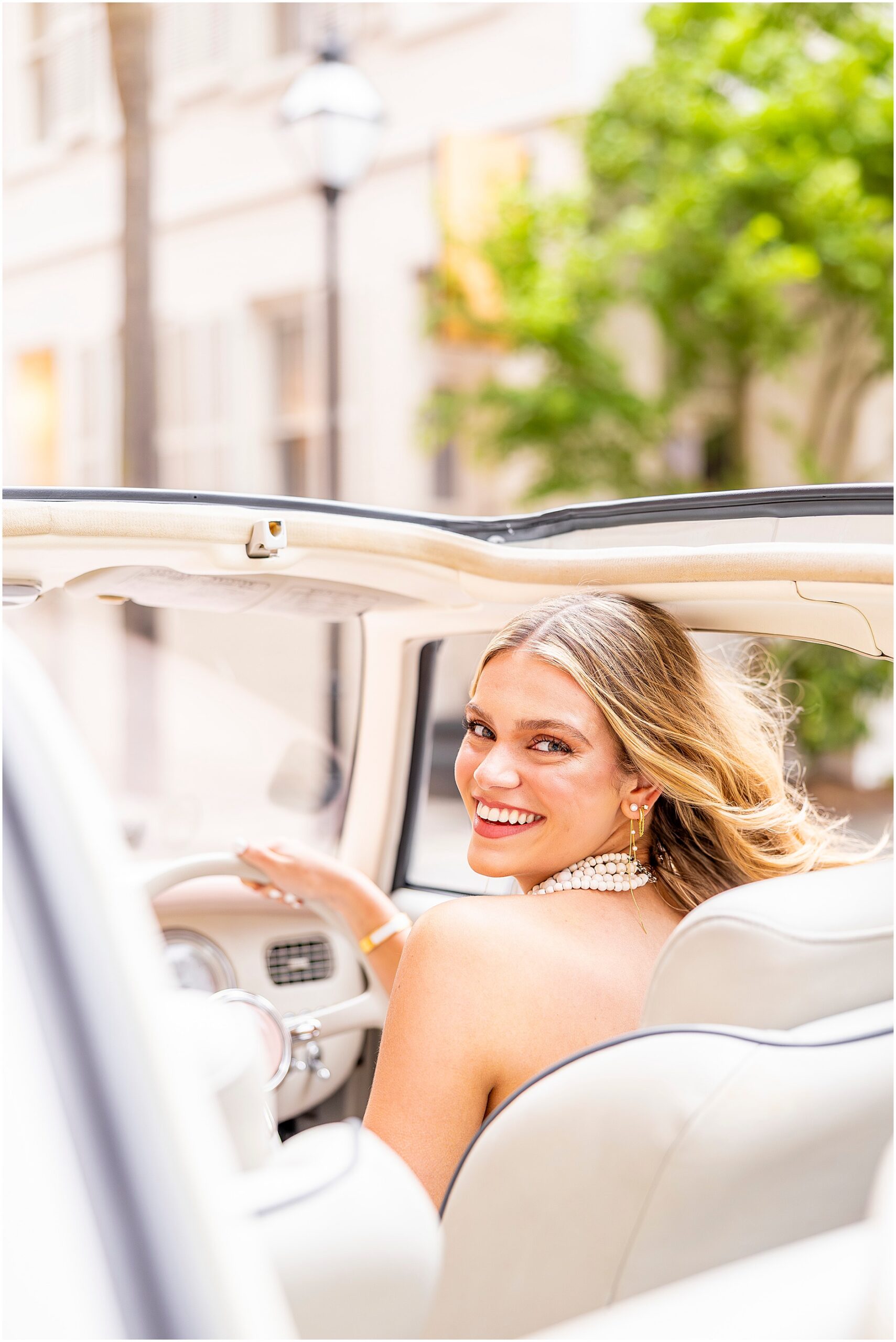 High school senior smiling over her shoulder as she poses in the drivers seat of The Pink Figgy during her Charleston senior photos