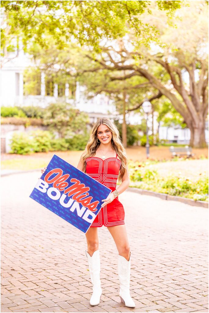 Senior photos in Washington Square Park Charleston with oak trees and greenery, holding an Ole Miss bound sign