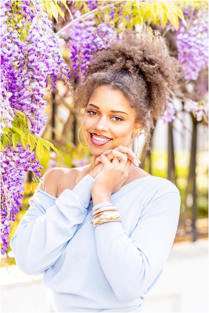 Senior girl in flowy outfit posing beneath wisteria in Charleston South Carolina