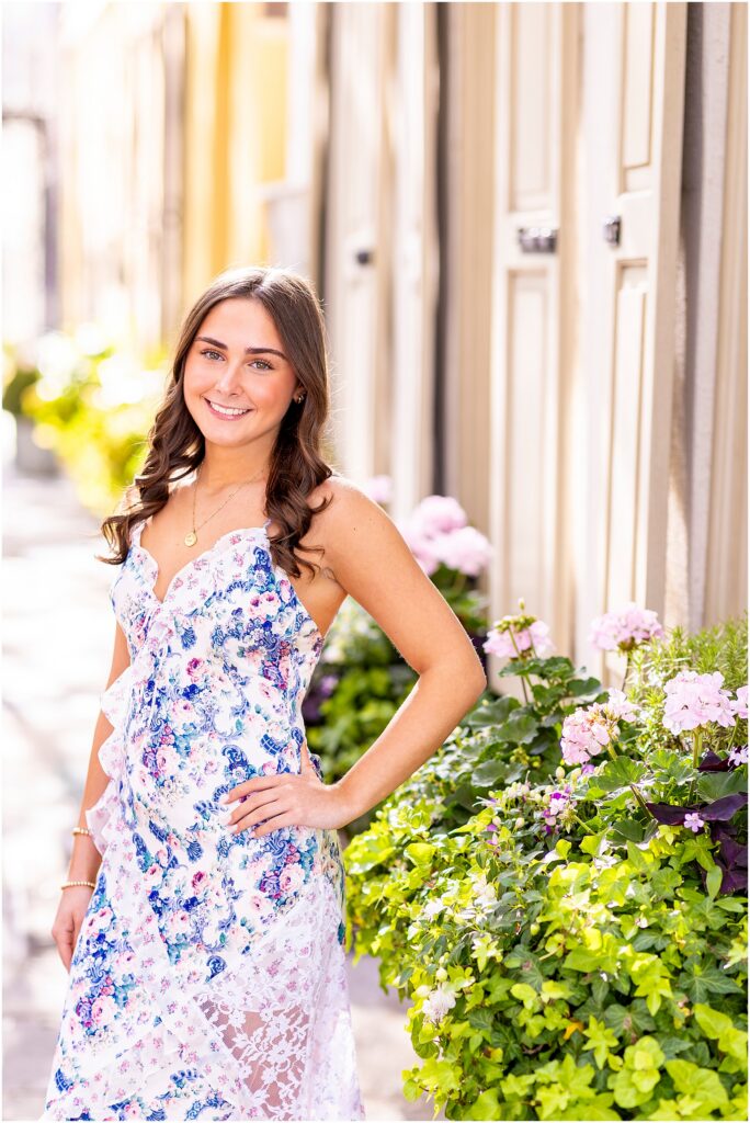 Senior girl posing with her hand on her hip in front of a window box with pink flowers on Tradd Street in Charleston, South Carolina for her senior portriats 