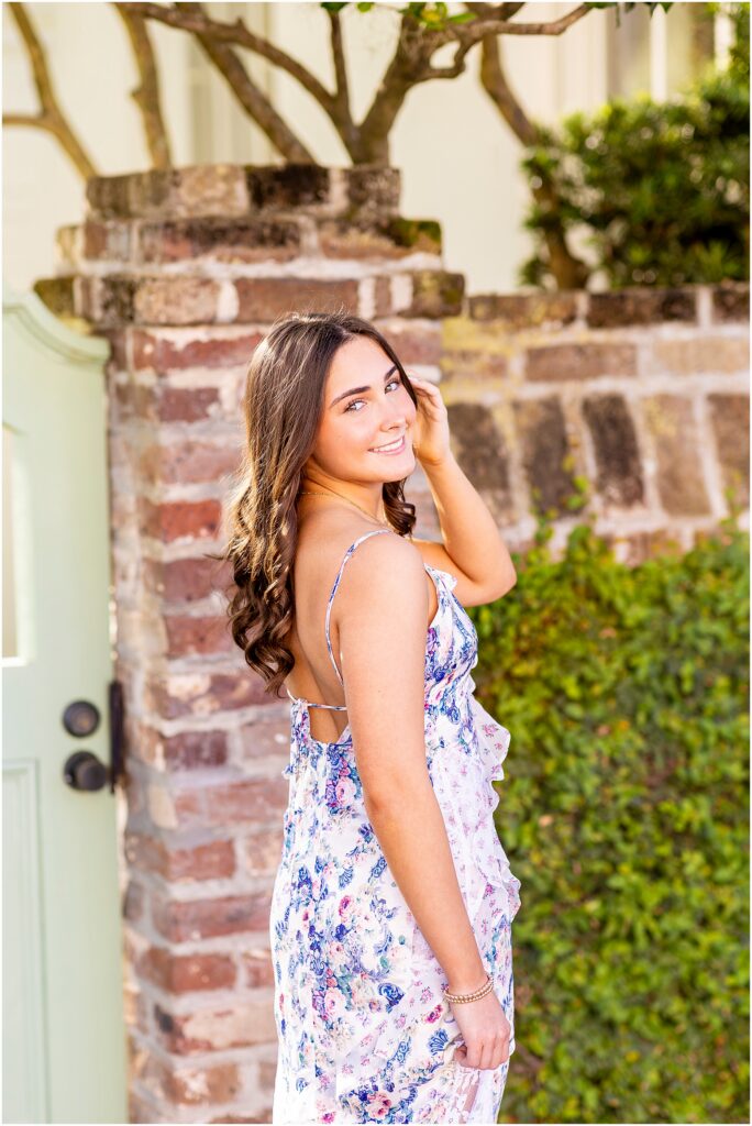 Senior girl posing with one hand in her hair as she looks over her shoulder in front of a green door along Rainbow Row in Charleston, SC