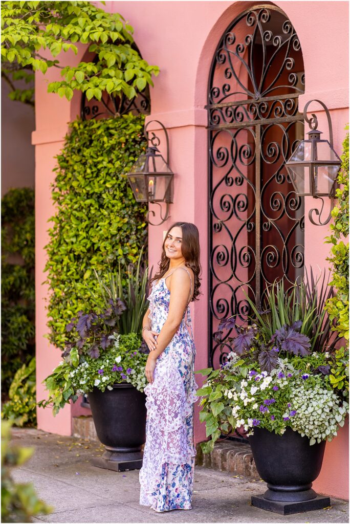 Charleston senior girl posing in front of a pink historic home on Rainbow Row with a black wired gate and greenery