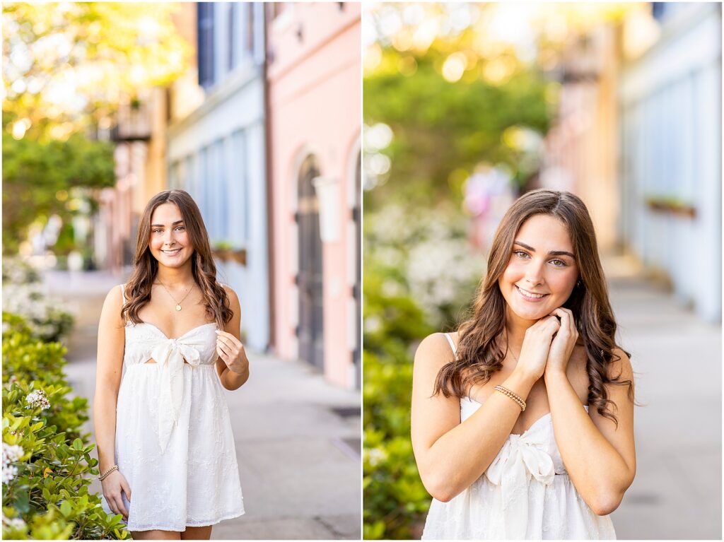 High school senior girl posing joyfully for her portraits with pastel homes and greenery on Rainbow Row in downtown Charleston