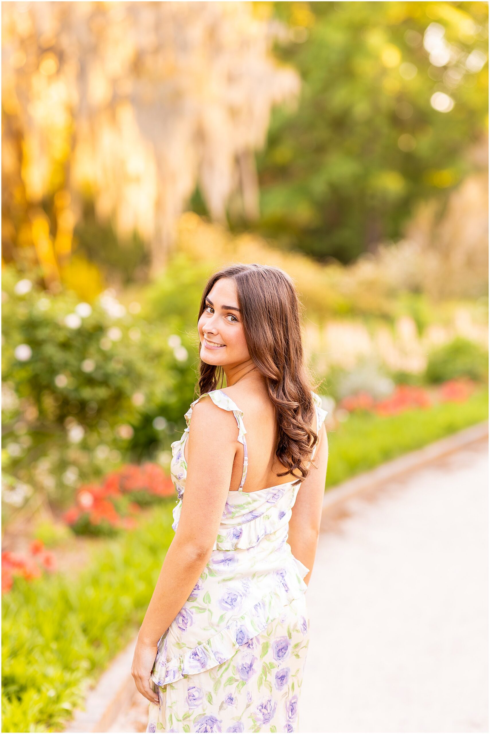 Senior girl looking over her shoulder for her photos in Hampton Park as she walks through the garden