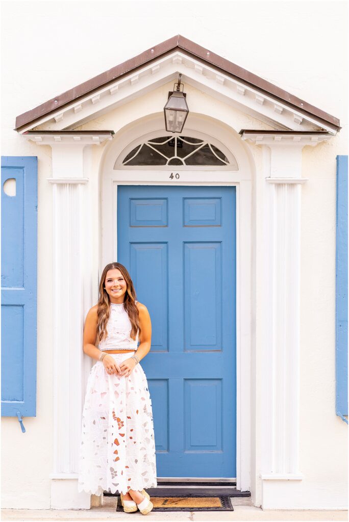 Girl in white dress posing in front of the iconic blue door on Tradd Street for her senior portriats