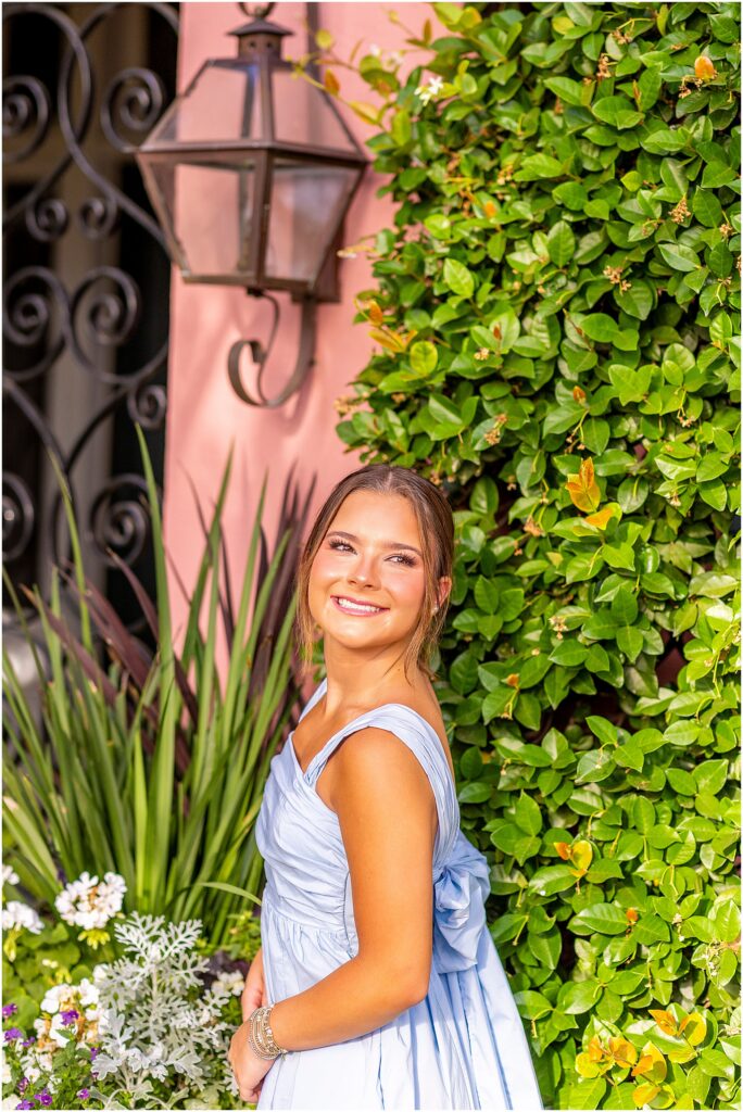 High school senior girl smiling off in the distance as she poses softly with greenery along Rainbow Row in Charleston
