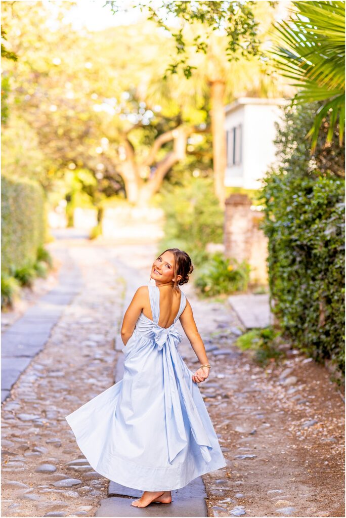 Charleston senior showing off her blue dress with big bow in the back as she spins on a downtown cobblestone street
