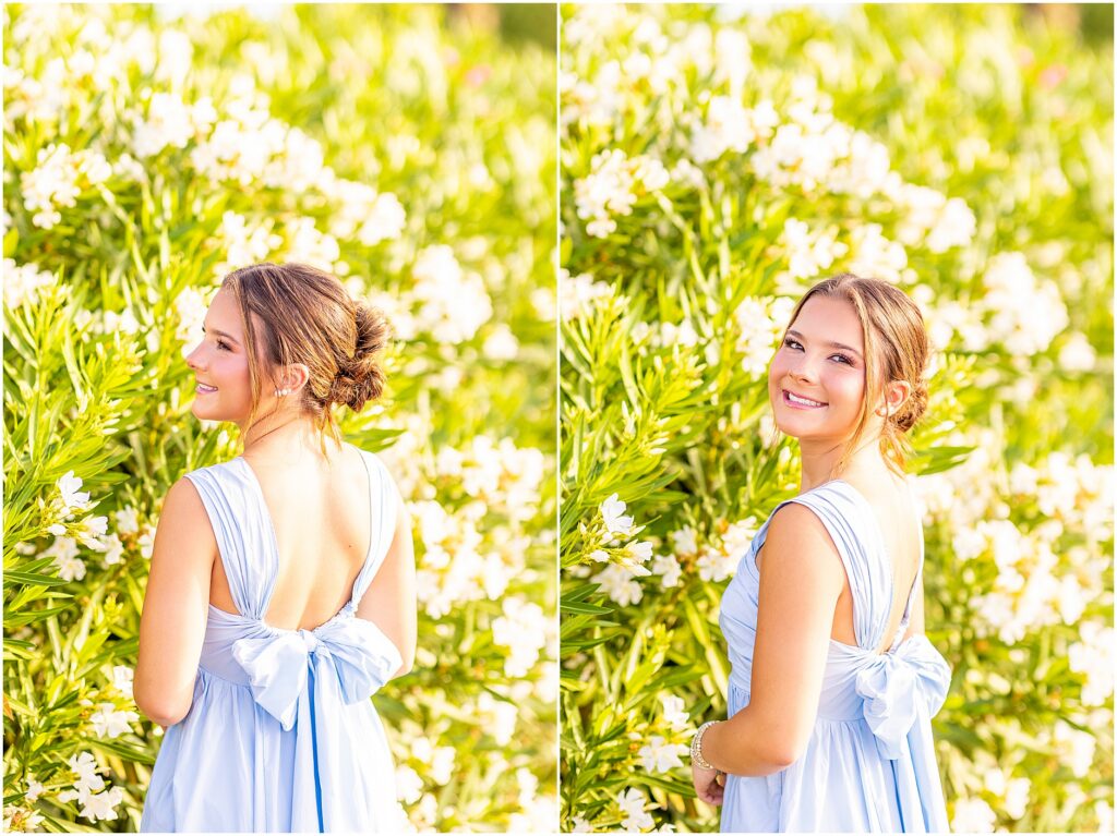Charleston senior smiling over her shoulder with white flowers as the backdrop and a big blue bow on her dress