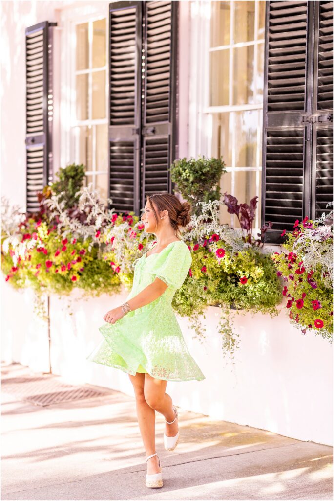 Senior girl twirling in a green dress with window boxes filled with florals behind her on Rainbow Row