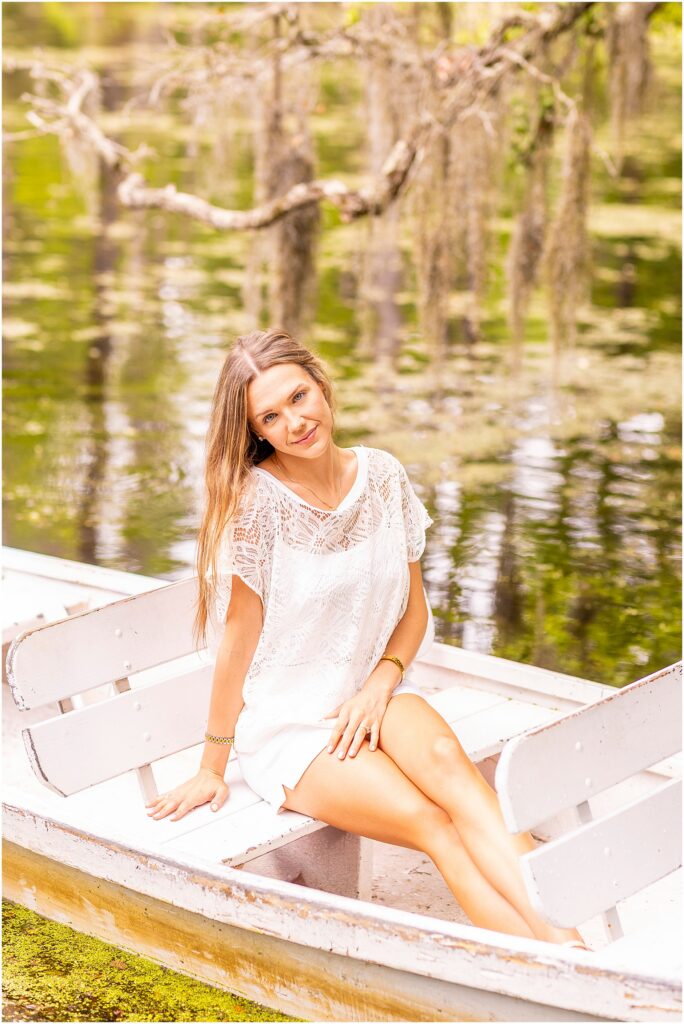 Graduate sitting in a wooden rowboat surrounded by cypress trees at Cypress Gardens