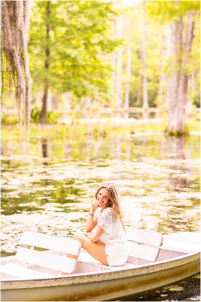 Charleston Southern University graduate sitting in a wooden rowboat surrounded by water and trees at Cypress Gardens.