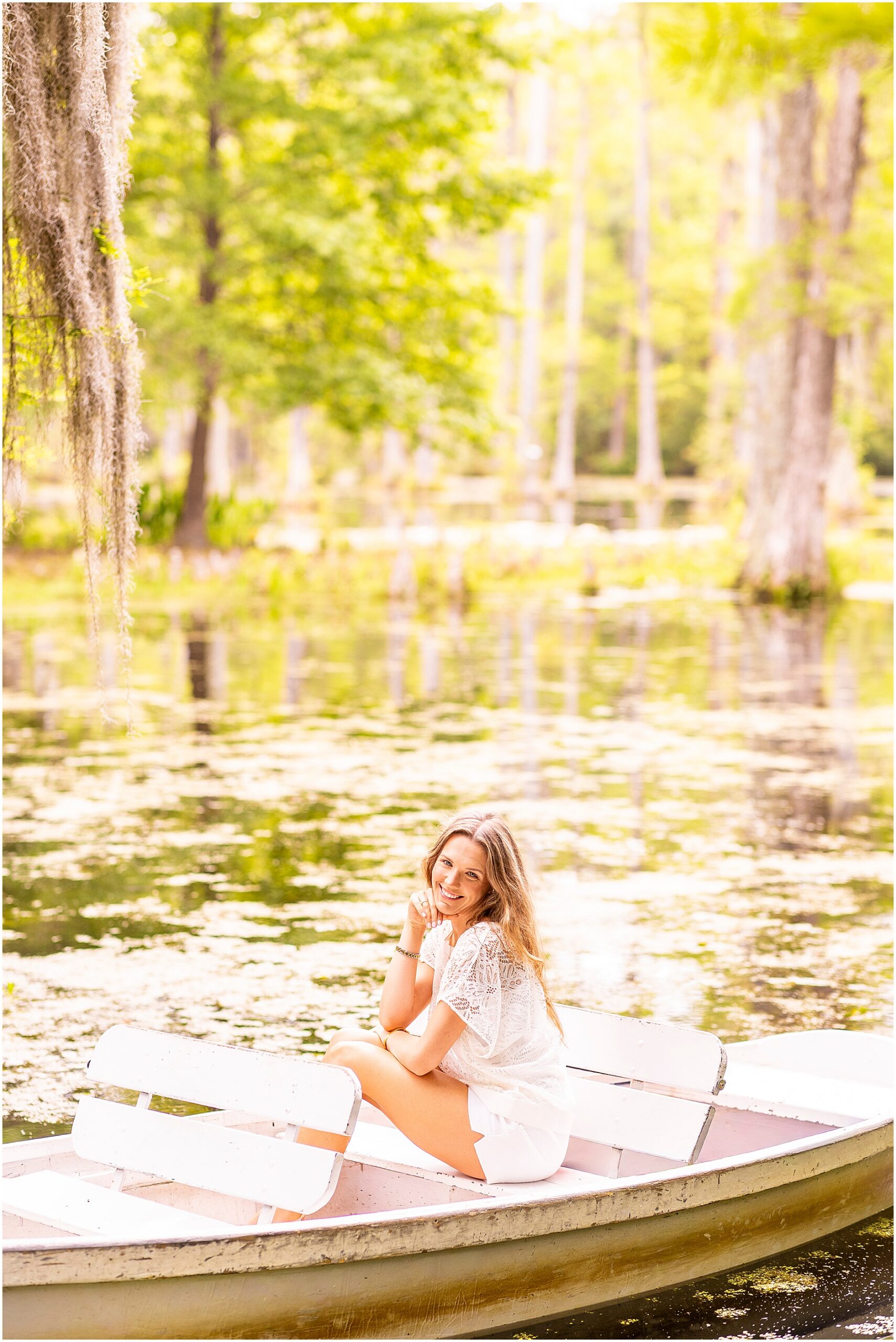 Charleston Southern University graduate sitting in a wooden rowboat surrounded by water and trees at Cypress Gardens.