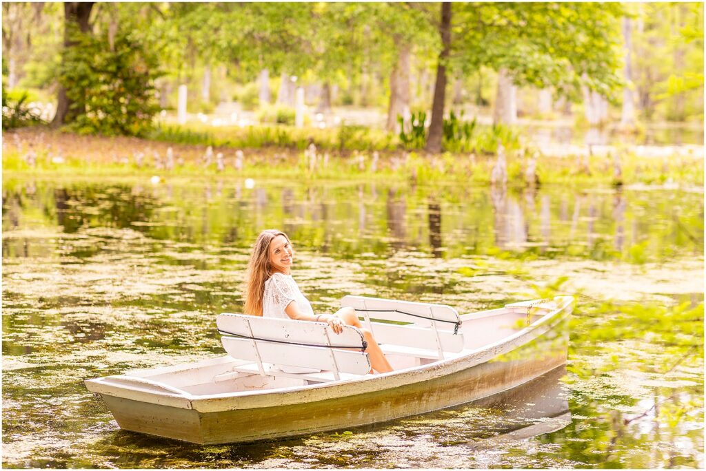 Senior looking over her shoulder as she sits in a rowboat floating in the water at Cypress Gardens for her college graduation photos