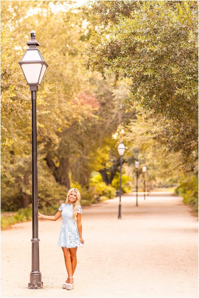 Senior girl posing among the trees at Hampton Park in a light blue dress with warm golden-hour light