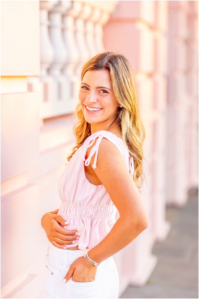Charleston senior portrait of a girl in a light pink top and white jeans in front of the pink mansion at The Battery