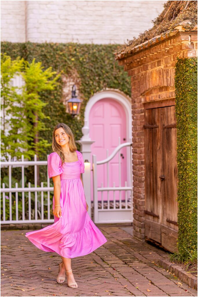 Senior girl in a bright pink dress posing along a charming South of Broad street in Charleston SC