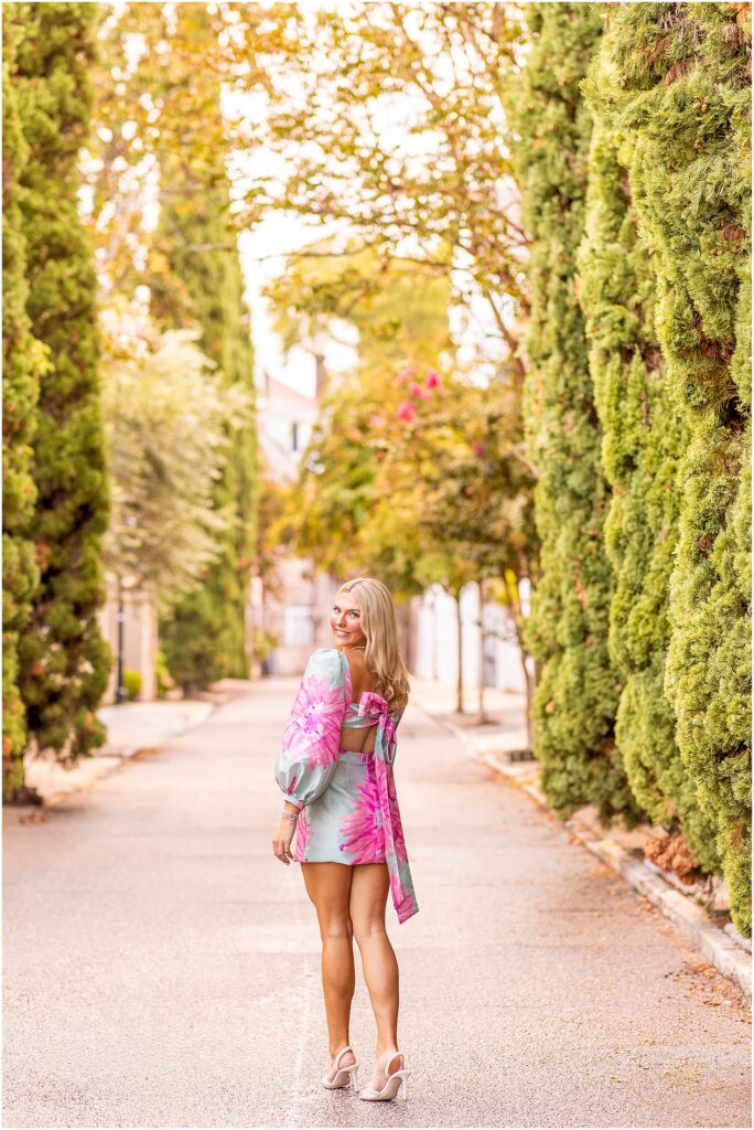 Senior girl in a vibrant blue and pink dress posing along the historic streets of South of Broad in Charleston SC