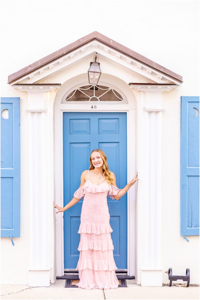 Feminine Charleston senior portrait of a girl in a pink dress surrounded by the pastel historic homes of Rainbow Row