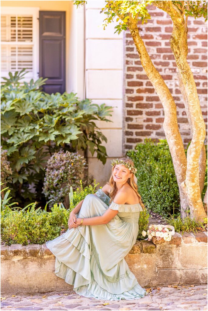 Elegant Charleston senior photos of a girl in a green dress and flower crown along the cobblestone streets of South of Broad